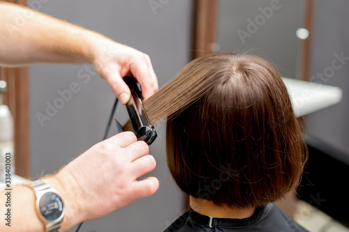 Hairdresser straightens hair of woman with hair straightener tool in hair salon.
