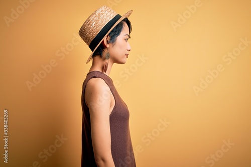 Young beautiful asian girl wearing casual t-shirt and hat over isolated yellow background looking to side, relax profile pose with natural face with confident smile. © Krakenimages.com