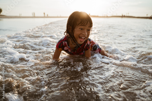 Fototapeta Naklejka Na Ścianę i Meble -  Asian little girl sitting on sand in the beach while playing water on a nice beach
