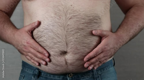 shirtless caucasian fat man slams and knocks by hands himself on the big belly which shakes like a drum