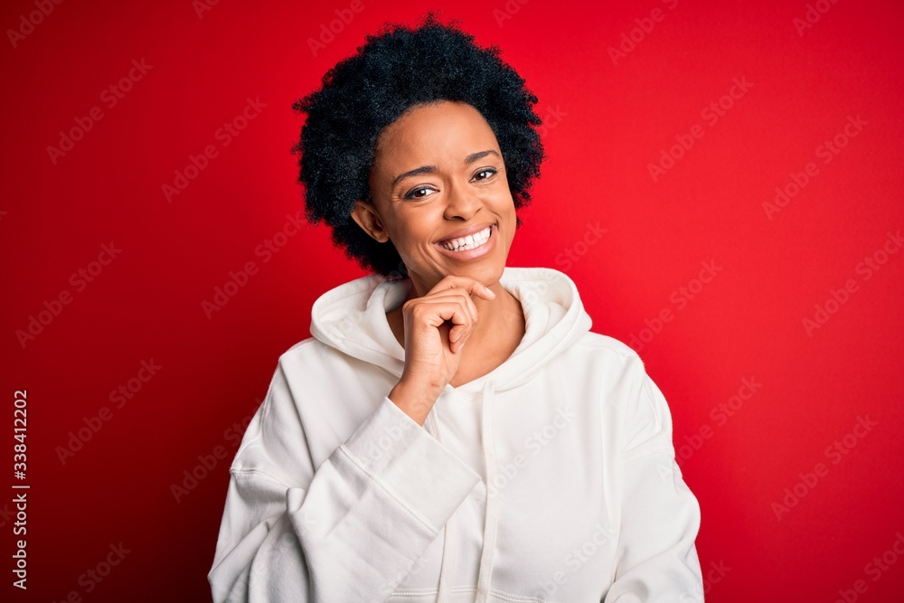 Young beautiful African American afro sportswoman with curly hair wearing sportswear looking confident at the camera with smile with crossed arms and hand raised on chin. Thinking positive. Young beautiful African American afro sportswoman with curly hair wearing sportswear looking confident at the camera with smile with crossed arms and hand raised on chin. Thinking positive.