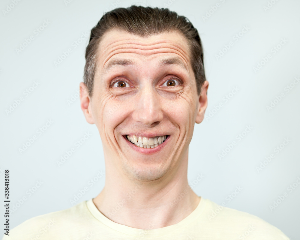 Fototapeta premium Portret mężczyzny z głupawym szerokim uśmiechem, szare tło, seria emocji
