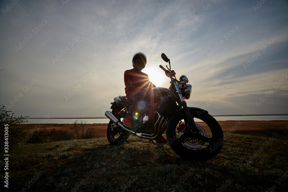 
young man and motorcycle at sunset near the water