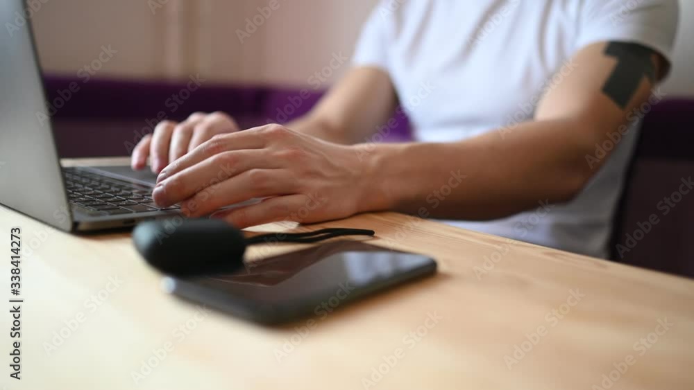 Unrecognizable man hands with smartphone and headphones working on a laptop during coronavirus isolation home quarantine. Covid-19 pandemic Corona virus. Distance online work from home concept. Unrecognizable man hands with smartphone and headphones working on a laptop during coronavirus isolation home quarantine. Covid-19 pandemic Corona virus. Distance online work from home concept.