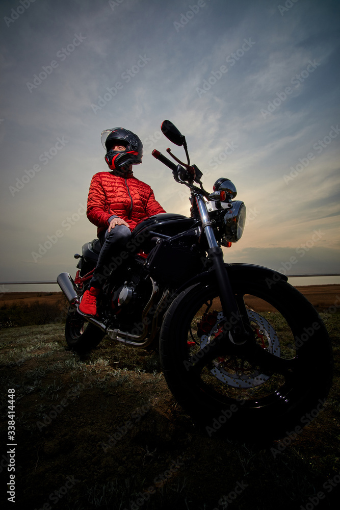 
young man and motorcycle at sunset near the water