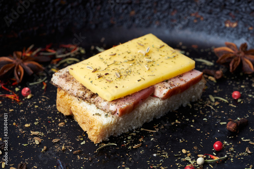 Closeup of a sandwich with brisket and cheese with spices on a dark background.