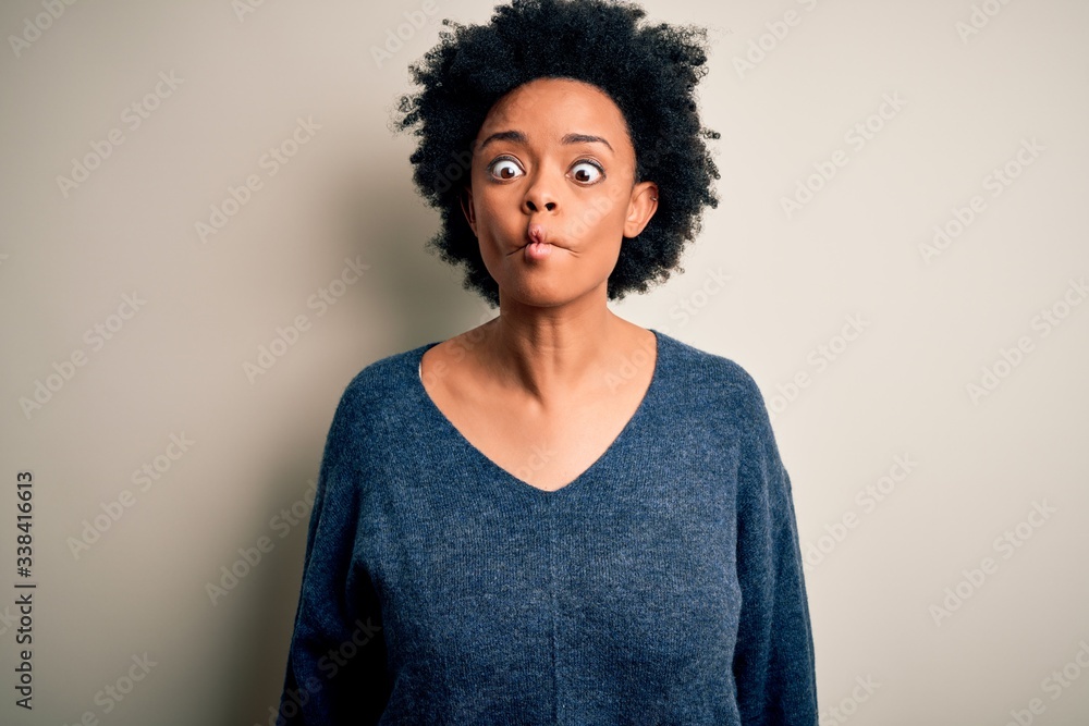 Young beautiful African American afro woman with curly hair wearing casual sweater making fish face with lips, crazy and comical gesture. Funny expression.