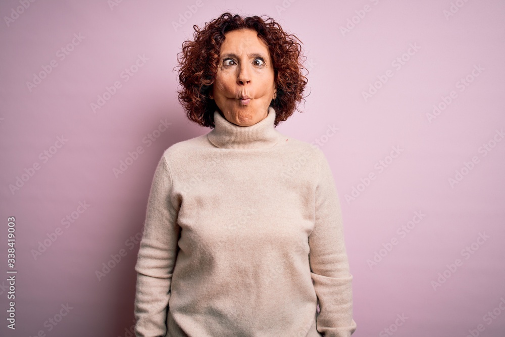 Middle age beautiful curly hair woman wearing casual turtleneck sweater over pink background making fish face with lips, crazy and comical gesture. Funny expression. Middle age beautiful curly hair woman wearing casual turtleneck sweater over pink background making fish face with lips, crazy and comical gesture. Funny expression.