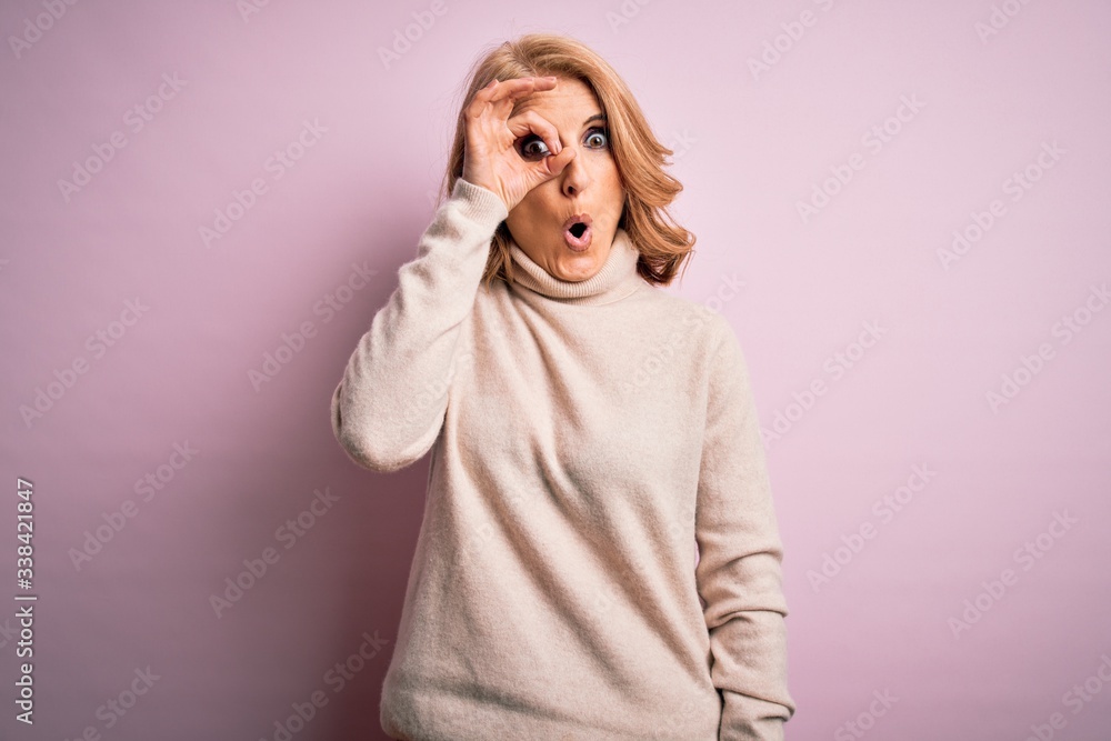 Middle age beautiful blonde woman wearing casual turtleneck sweater over pink background doing ok gesture shocked with surprised face, eye looking through fingers. Unbelieving expression. Middle age beautiful blonde woman wearing casual turtleneck sweater over pink background doing ok gesture shocked with surprised face, eye looking through fingers. Unbelieving expression.