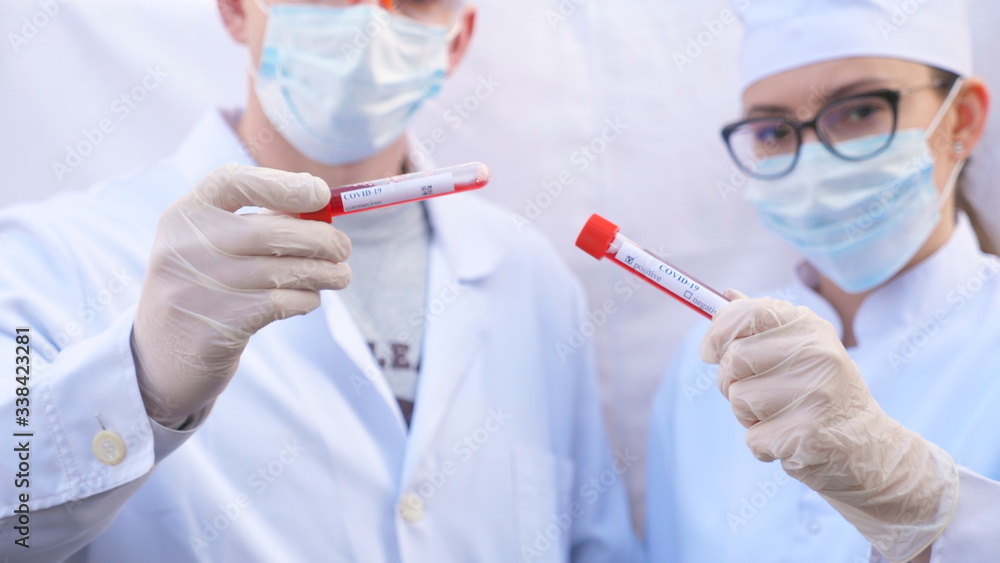 Male and female doctors holds test tube with blood sample to coronavirus. Two medics with protective gloves and glasses tests blood samples. Concept of health and safety life from COVID-19 pandemic Male and female doctors holds test tube with blood sample to coronavirus. Two medics with protective gloves and glasses tests blood samples. Concept of health and safety life from COVID-19 pandemic