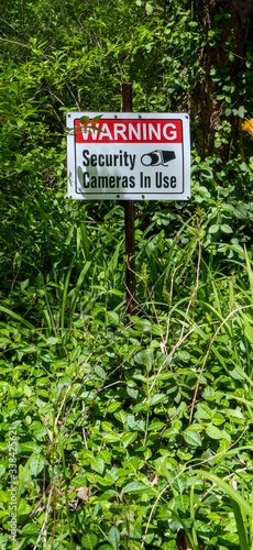 SECURITY CAMERAS IN USE Sign in vine covered woods.
