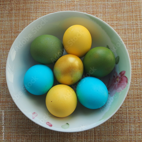 Colorful Easter eggs lie in a white porcelain plate. Blue, green, yellow, Golden eggs.