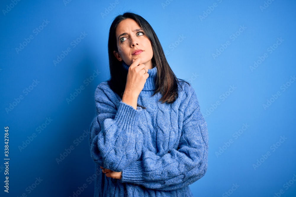 Young brunette woman with blue eyes wearing casual turtleneck sweater with hand on chin thinking about question, pensive expression. Smiling with thoughtful face. Doubt concept. Young brunette woman with blue eyes wearing casual turtleneck sweater with hand on chin thinking about question, pensive expression. Smiling with thoughtful face. Doubt concept.