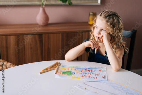 Thoughtful girl thinking about what picture do drawing with colorful pencil at the table in cozy children's room. Concept of child creative activity.