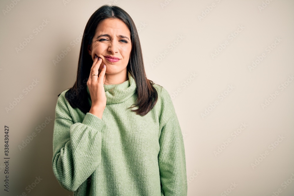 Fototapeta premium Young brunette woman with blue eyes wearing turtleneck sweater over white background touching mouth with hand with painful expression because of toothache or dental illness on teeth. Dentist