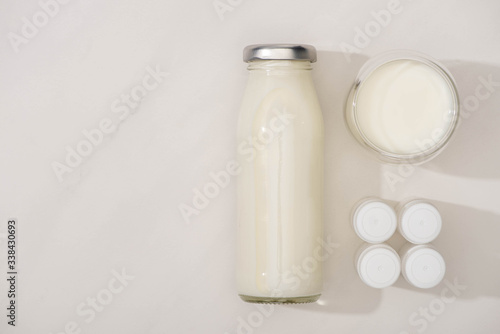 Top view of bottle and glass of homemade yogurt near containers with starter cultures on white background