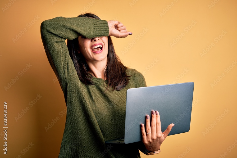 Young brunette woman with blue eyes working using computer laptop over yellow background Smiling cheerful playing peek a boo with hands showing face. Surprised and exited Young brunette woman with blue eyes working using computer laptop over yellow background Smiling cheerful playing peek a boo with hands showing face. Surprised and exited