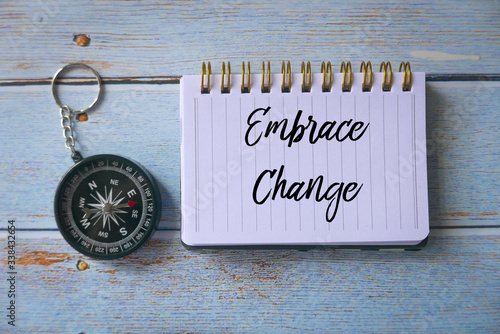 Canvastavla Top view of compass and notebook written with Embrace Change on wooden background