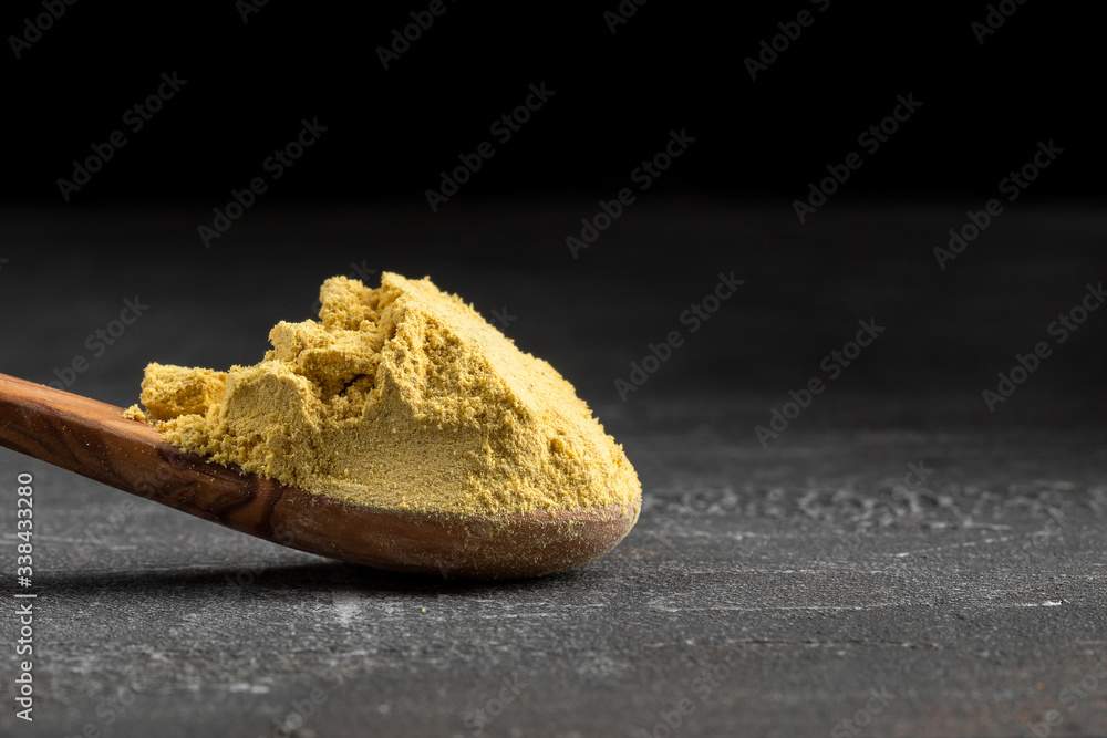 Side view on yellow dried ground mustard powder in the wooden spoon on the grey background, horizontal format