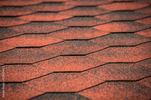 Red asphalt bitumen shingles roof tiles closeup background. Selective focus. Roofing construction.