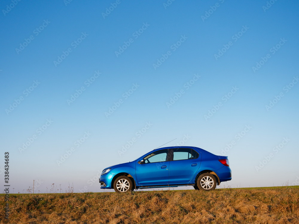 Fototapeta premium Belarus blue car in a field in spring at sunrise