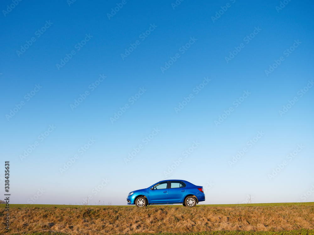 Fototapeta premium Belarus blue car in a field in spring at sunrise