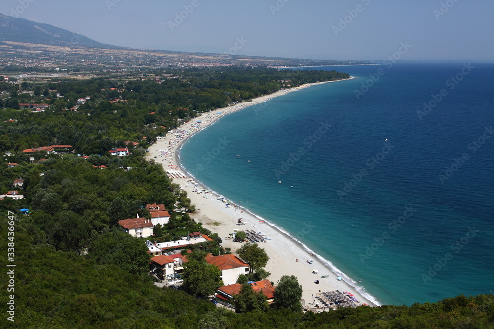 A beach of white sand between the green coast and the blue sea. View from above