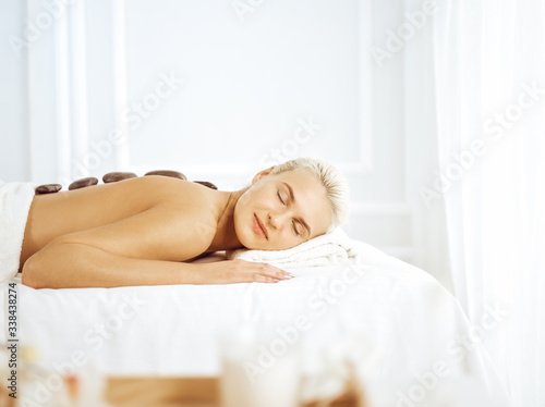 Beautiful blonde woman enjoying warm stones procedure with closed eyes. Spa concept