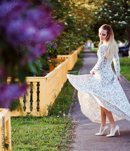 Beautiful woman is dancing with her dress outdoors in spring in countryside. Blooming flofers in front of the woman. Lilac bush.  photo