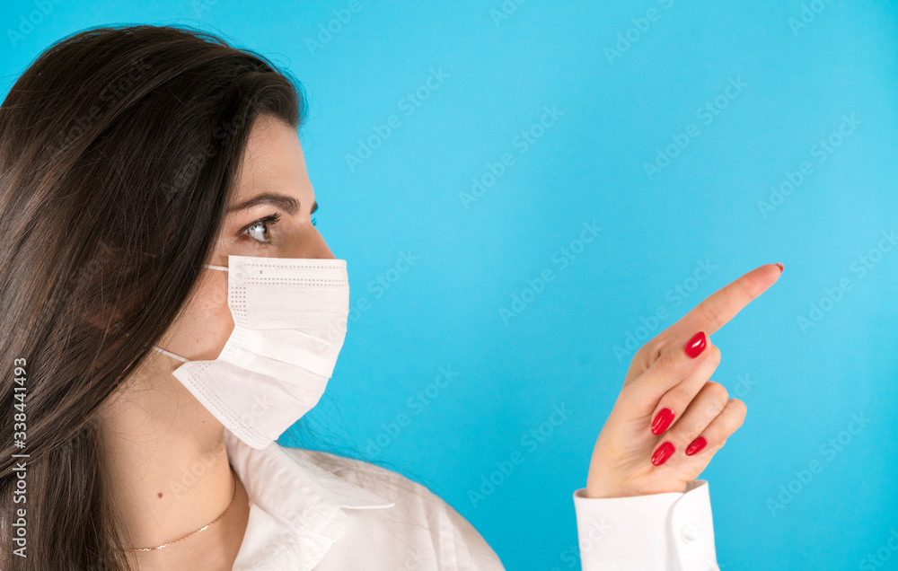 Horizontal shot of beautiful dark haired woman wearing medical disposable mask pointing with index finger. Horizontal shot of beautiful dark haired woman wearing medical disposable mask pointing with index finger.
