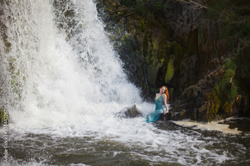 beautiful red-haired girl bathes in a stormy stream of a waterfall  hot summer