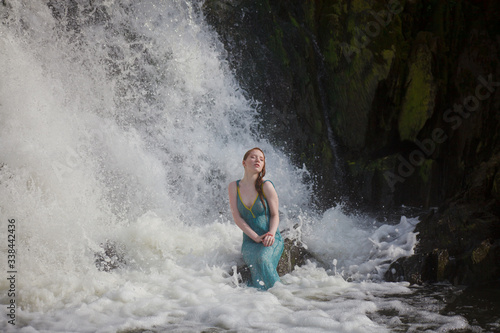 beautiful red-haired girl bathes in a stormy stream of a waterfall, hot summer
