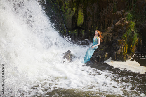 beautiful red-haired girl bathes in a stormy stream of a waterfall, hot summer