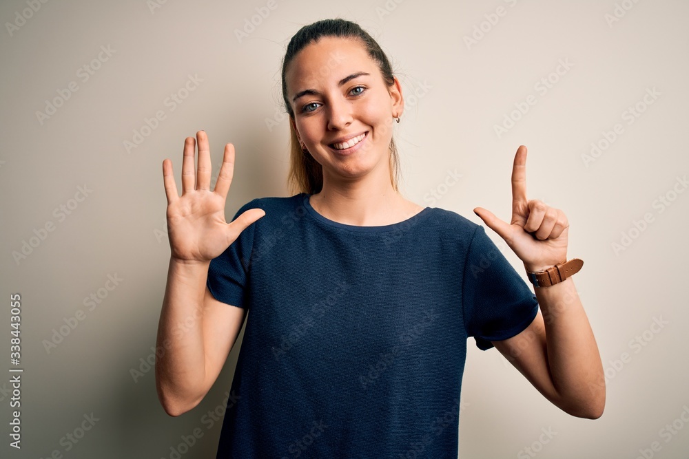 Young beautiful blonde woman with blue eyes wearing casual t-shirt over white background showing and pointing up with fingers number seven while smiling confident and happy. Young beautiful blonde woman with blue eyes wearing casual t-shirt over white background showing and pointing up with fingers number seven while smiling confident and happy.