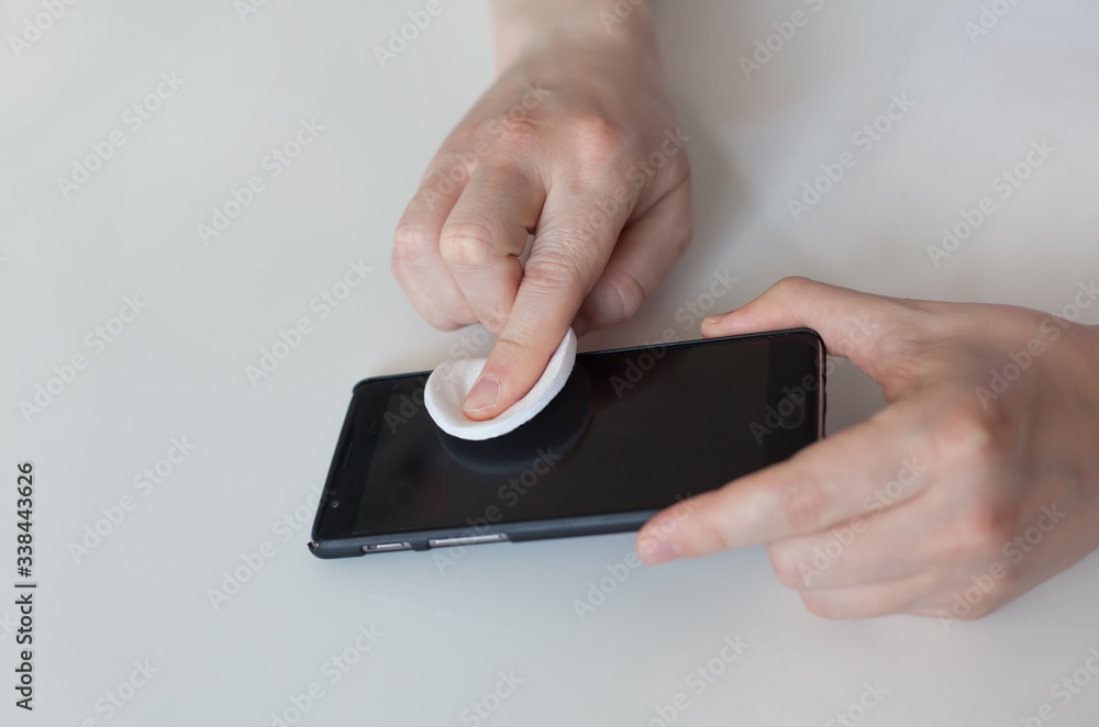 Man wiping his cell phone with cotton pad. Disinfection during covid 19 or coronavirus quarantine Man wiping his cell phone with cotton pad. Disinfection during covid 19 or coronavirus quarantine