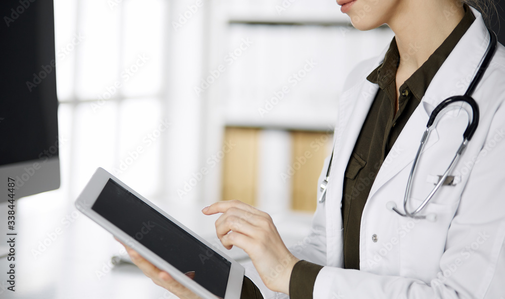 Unknown female doctor using tablet computer in clinic. Perfect medical service in hospital. Medicine concept Unknown female doctor using tablet computer in clinic. Perfect medical service in hospital. Medicine concept