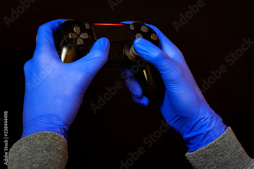 HANDS WITH LATEX GLOVES HOLDING A VIDEO CONSOLE CONTROL. VIRUS PREVENTION AT HOME