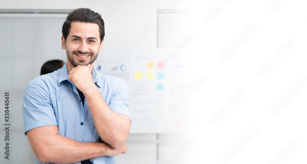 Confidence team leader. Young man owner startup business keeping arms crossed and looking at camera with smile while his colleagues working in the background Confidence team leader. Young man owner startup business keeping arms crossed and looking at camera with smile while his colleagues working in the background