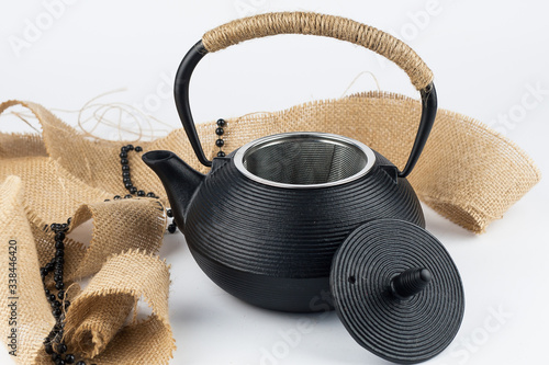 Closeup of open black teapot with rope on handle and sackcloth on white background.