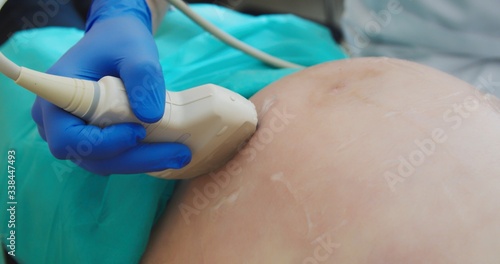 Ultrasound examination in doctors office. Close up shot on the ultrasound transducer on mothers belly