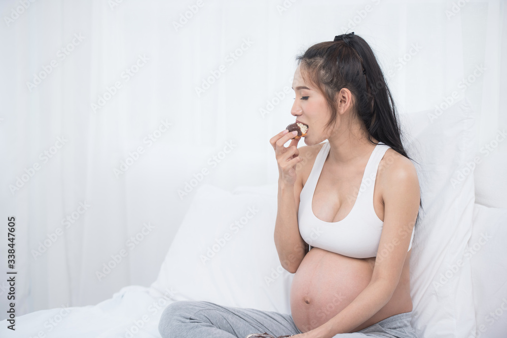 beautiful young pregnant woman holding sweet donut in her hand. expectation of the child, pregnancy and motherhood. healthy and unhealthy eating concept, diet. Junk food. soft focus background beautiful young pregnant woman holding sweet donut in her hand. expectation of the child, pregnancy and motherhood. healthy and unhealthy eating concept, diet. Junk food. soft focus background