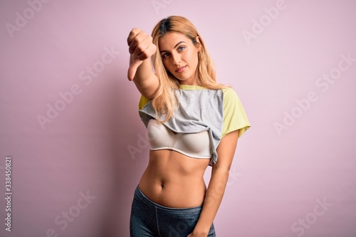 Young beautiful blonde sportswoman doing sport wearing sportswear over pink background looking unhappy and angry showing rejection and negative with thumbs down gesture. Bad expression. © Krakenimages.com