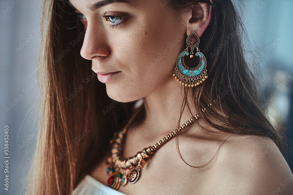 Fotka „Portrait of stylish sensual brunette boho woman with beautiful eyes  wearing big earrings and gold necklace. Fashionable indian hippie gypsy  bohemian outfit with jewelry details accessories“ ze služby Stock | Adobe