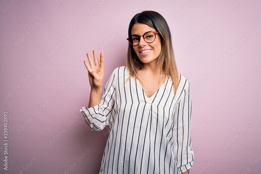 Young beautiful woman wearing casual striped t-shirt and glasses over pink background showing and pointing up with fingers number four while smiling confident and happy. Young beautiful woman wearing casual striped t-shirt and glasses over pink background showing and pointing up with fingers number four while smiling confident and happy.