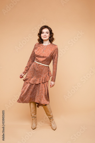 Beautiful young female with short dark hair, pretty face in long orange dress, ocher color long boots smiles