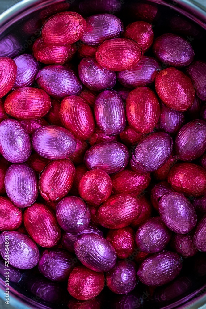 A top down close up portrait of a bunch of colorful chocolate easter eggs wrapped in tin foil lying on top of each other lying in a metal pot. Ready to be eaten. They are purple and red colored. A top down close up portrait of a bunch of colorful chocolate easter eggs wrapped in tin foil lying on top of each other lying in a metal pot. Ready to be eaten. They are purple and red colored.