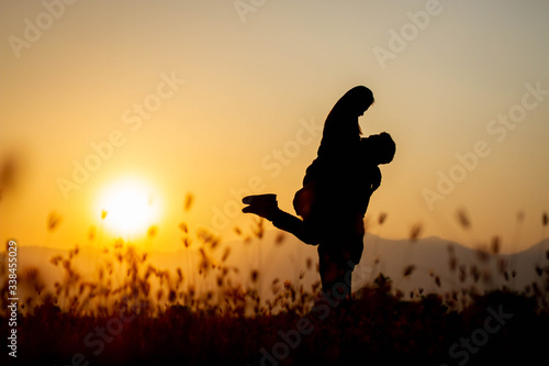 The shadow of a backlit lover who is hugging each other happily at sunset with grass.