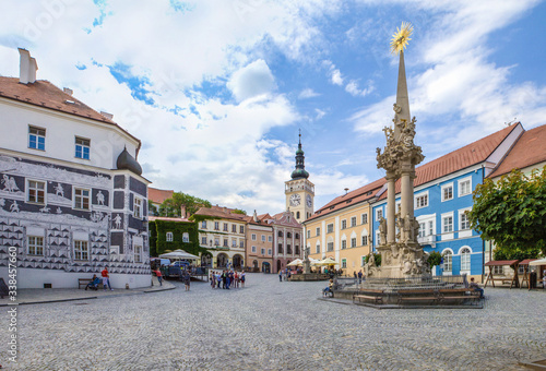 MIKULOV, CZECH REPUBLIC - JUNE 16, 2019: Mikulov - Main square, statue of the Holy Trinity and graffiti house "U Rytířů". St. Wenceslav Church with Renaissance Tower in the background.