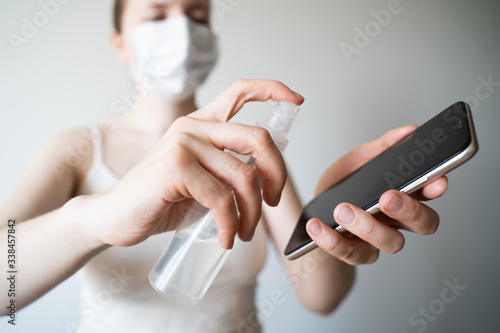Cleaning mobile phone to eliminate germs, coronavirus Covid-19. Woman hands cleaning smartphone by alcohol hand sanitizer and wipe with cloth