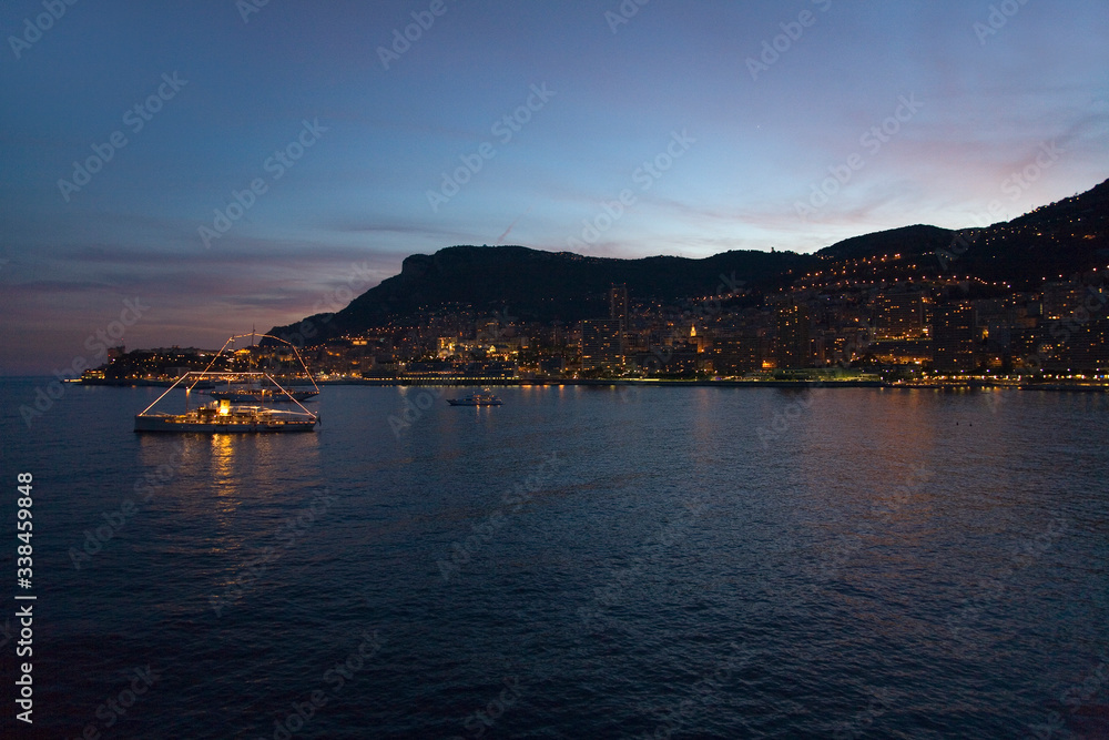 Yacht and seaside night view of Monte-Carlo with lights at dusk, in the Principality of Monaco, Western Europe on the Mediterranean Sea